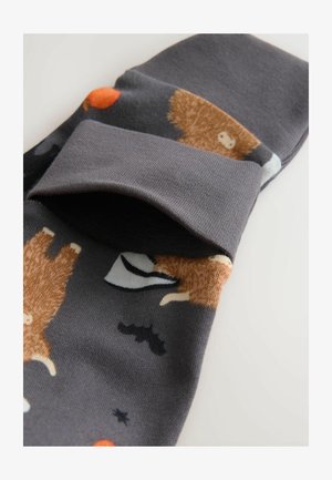 Calze grigie con motivi di animali giocosi, che presentano orsi marroni, pipistrelli neri e punti arancioni, arrotolate sul polsino.