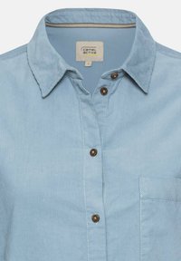 Chemise en velours côtelé bleu clair avec boutons marron, col pointu, poche poitrine et étiquette "camel active" à l'intérieur du col, taille petite.