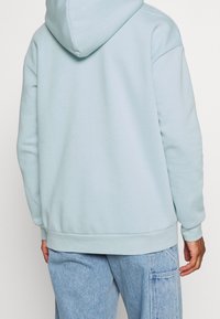 Sudadera con capucha azul claro de textura suave, con una capucha espaciosa, puños acanalados y un dobladillo recto, combinada con pantalones vaqueros claros.