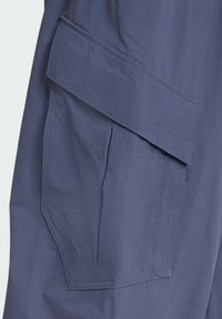 Pantalones cargo en una tela azul oscura. Presentan un gran bolsillo en ángulo en el lado. Textura suave con detalles de costura sutiles.