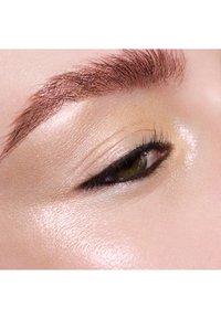 Nahaufnahme eines menschlichen Auges mit definierten Wimpern, hellbraunem Iriss, ausgeformten Brauen und glatter, strahlender Haut mit warmen Untertönen.