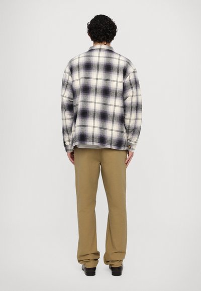 Plaid flannel shirt in white and purple tones, featuring a relaxed fit and long sleeves. Paired with beige trousers and black shoes.