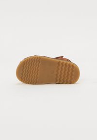 Brun sandal med en teksturert gummisåle som har et sikksakkmønster, med justerbare reimer og et solid design.