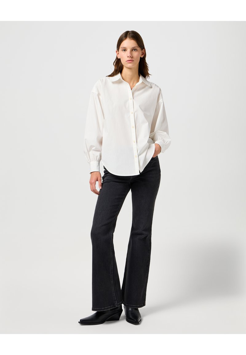 Witte shirt met knoopsluiting en een klassieke kraag, lange mouwen en details op de manchetten, gecombineerd met donker flare jeans en zwarte wedge laarzen.