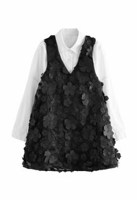 Schwarzes ärmelloses Kleid mit 3D-Blütenapplikationen, über einem weißen Langarmshirt getragen. Verfügt über einen V-Ausschnitt und strukturierte Verzierungen.