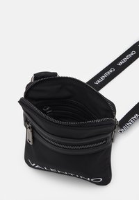 Svart nylon crossbody-väska med silverfärgad hårdvara, blixtlåsstängningar och en justerbar rem med "VALENTINO"-logotyp. Interiören har flera fack.