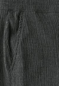 Svart texturerad tyg med ett veckat mönster. Har en slät midjeband och en sidficka, med ett linjärt mönster genom hela tyget.
