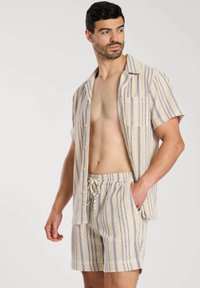 Kortärmad, knäppt skjorta och matchande shorts gjorda av lätt vävt tyg. Krämfärgad bas med blå randmönster, med en framficka.