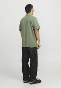 Polo shirt verde a maniche corte abbinato a pantaloni in denim scuri. La maglietta ha una vestibilità comoda, mentre i pantaloni presentano una forma dritta e cuciture in vista.
