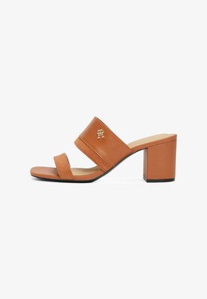 Tan leather block-heeled sandal with two straps, showcasing a gold logo accent and a smooth texture. Open-toe design.