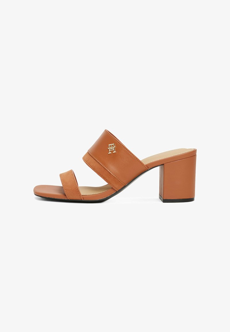 Sandale à talon bloc en cuir tan avec deux sangles, mettant en valeur un accent de logo doré et une texture lisse. Design à bout ouvert.