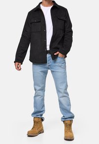 Czarna kurtka z polaru z dwoma kieszeniami na piersiach, noszona na białej koszulce. Jasnoniebieskie dżinsy i jasnobeżowe botki do kostki dopełniają strój.