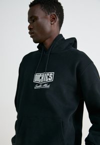 Felpa nera con cappuccio realizzata in cotone, con il logo bianco "Dickies" e il testo "Quality Made" sul petto, dotata di tasca frontale.