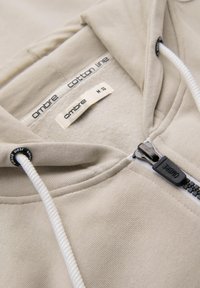 Felpa beige in cotone con zip anteriore e cordoncino. Le etichette riportano "ombre" e "cotton line", taglia M, con una texture morbida.