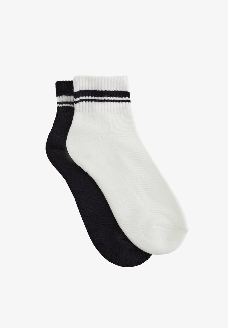 Par de calcetines tobilleros, uno blanco y otro negro, ambos con dos finas rayas negras cerca del puño, sobre un fondo blanco liso.