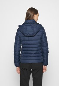 Chaqueta de puffer azul marino con capucha desmontable, diseño acolchado y costuras horizontales. Material ligero con una textura suave.