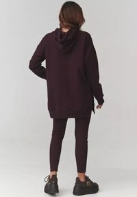 Bordowa, oversize bluza z kapturem, z prążkowanymi mankietami i rozcięciami po bokach, w połączeniu z dopasowanymi legginsami i masywnymi czarnymi sneakersami.