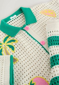 Cardigan crème en crochet avec col vert, boutons roses, broderie de palmier et fruits d'agrumes, et manches à rayures vertes.