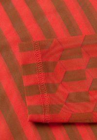 Rood en bruin geborduurd stof met een geometrisch patroon. Het heeft afwisselende strepen, een gladde textuur en gestikte randen.