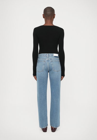 Top negro de manga larga combinado con jeans rectos de pernera clara, que presentan un diseño de cinco bolsillos y una etiqueta blanca en la parte trasera.
