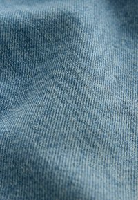 Gros plan sur un tissu en denim bleu texturé avec un motif de trame diagonale visible et des plis subtils.