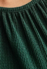 Ciemnozielony teksturowany materiał z plisowanym wzorem, przedstawiający spójny deseń i miękką, lekko pomarszczoną powierzchnię.