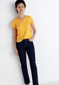 Geel V-hals T-shirt van katoen, gecombineerd met donkerblauwe rechte jeans. De outfit heeft een casual pasvorm en geen zichtbare patronen.