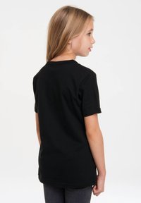 Schwarzes Kurzarm-T-Shirt aus Baumwolle mit Rundhalsausschnitt, glatter Textur und lockerer Passform. Von einem Kind getragen, von hinten gesehen.