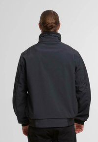 Black, padded jacket with high collar, elastic cuffs, and adjustable drawstring at neck. Smooth texture with a sleek, minimalist design.