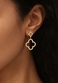Gold drop earrings featuring a layered quatrefoil design with cut-out shapes. Polished metal surface, hanging from a stud attachment.
