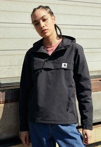 Giacca nera a pullover con cappuccio, tasca frontale e dettagli con zip. Realizzata in materiale liscio, presenta una piccola etichetta con logo sul petto.
