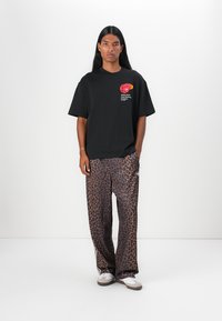 Sort oversized t-shirt med logodetalje; parret med løse leopardmønstrede bukser. Modellen har hvide sneakers med brune accenter på.