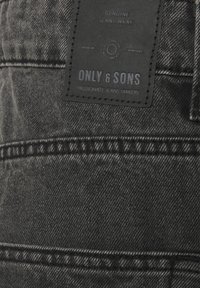 Musta denimpäällinen, jossa on teksturoidun pinnan rakenne. Vyötärönauhassa ommeltu suorakulmainen nahkainen merkki, jossa on kohokuvioitu bränditeksti.