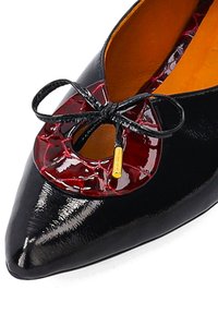 Czarne lakierowane buty z końcem w szpic, z przyciętym czerwonym teksturowanym akcentem oraz czarną kokardką przy otworze.