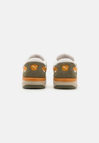 Sneaker in suede marrone con accenti in tessuto bianco e dettagli arancioni. Tallone arrotondato, superficie testurizzata e dettaglio del logo sul retro.
