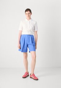 Vit polo skjorta, blå shorts med veck och rosa sneakers. Outfiten har en knappdetalj på shortsen och en logotyp på skjortan.