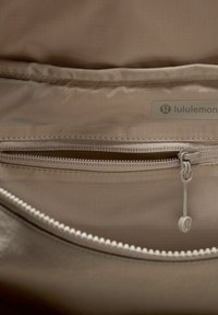 Beige Lululemon-väska med ett inre fack som har en dragkedja och en texturerad tygbeklädnad, samt en grå etikett på utsidan högst upp.