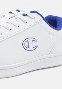 Vita syntetiska sneakers med blå accenter, med en rund logotyp på sidan, snörningsdesign och texturerad gummisula.