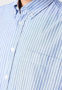 Gros plan d'une chemise à rayures verticales bleues et blanches avec une poche poitrine et un col boutonné.