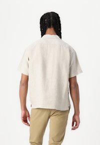 Korte mouwen lichtbeige shirt gemaakt van textuur stof, met een kraaglijn en een rechte zoom, gecombineerd met licht kaki broek.
