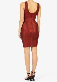 Donna che indossa un vestito rosso senza maniche, lungo fino al ginocchio, con un motivo testurizzato e zip sul retro, abbinato a sandali neri con tacco a stelo sferico.