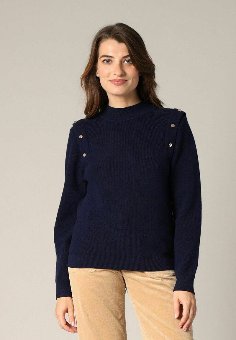 Pull en maille marine avec un col montant, des manches longues et des boutons décoratifs dorés aux épaules. Texture lisse et silhouette cintrée.