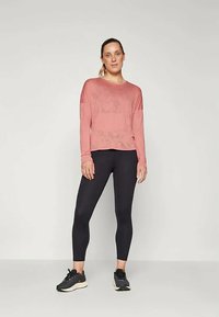 Langermet, lys rosa treningsgenser kombinert med svarte leggings og svarte joggesko. Stoffet ser mykt ut med en avslappet passform.