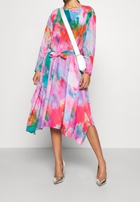 Vestido colorido de manga larga, con cintura ajustable y un estampado floral abstracto en rosa, verde y azul. Combinado con tacones altos plateados.