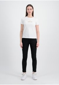 Hvit bomull t-skjorte med korte ermer, med metallisk tekst og stjernedesign. Kombinert med svart slim-fit bukser og hvite sneakers.