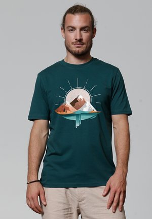 Dark teal t-shirt featuring a mountain graphic, with brown and white peaks, surrounded by a circular sunset design and rays emanating outward.