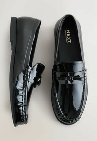 Sorte patenterede lædersko i loafer-stil med en rund tå, der har sløjfeakcenter og dekorativ syning langs siderne. Glat, skinnende finish.