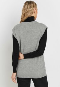 Maglione senza maniche grigio chiaro con una trama morbida, caratterizzato da un colletto rotondo e cuciture sulle spalle che cadono leggermente sopra le braccia.