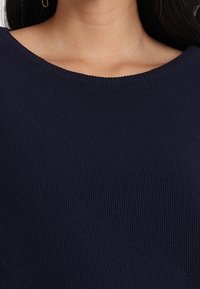 Marinblått stickat tröja med en bred rund halsringning och en texturerad tyg. Designen har en slät finish och subtila ribbade kanter.