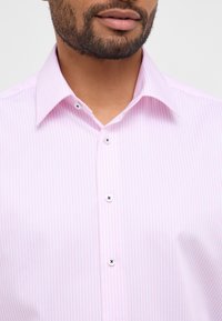 Camicetta rosa chiaro con righe bianche verticali, colletto button-down e bottoni neri a contrasto sulla patta anteriore.